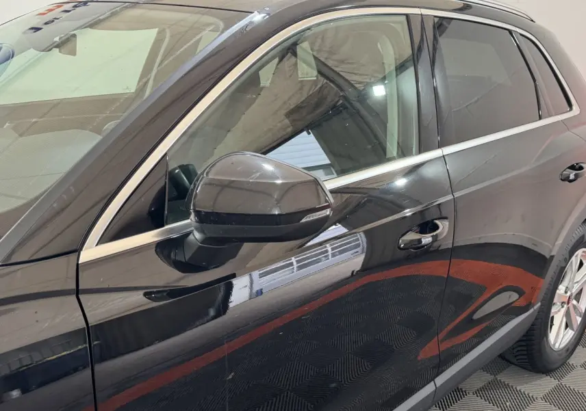 Vue latérale côté gauche d’un Audi Q3 noir 2022 avec rétroviseur et poignées de porte chromées.