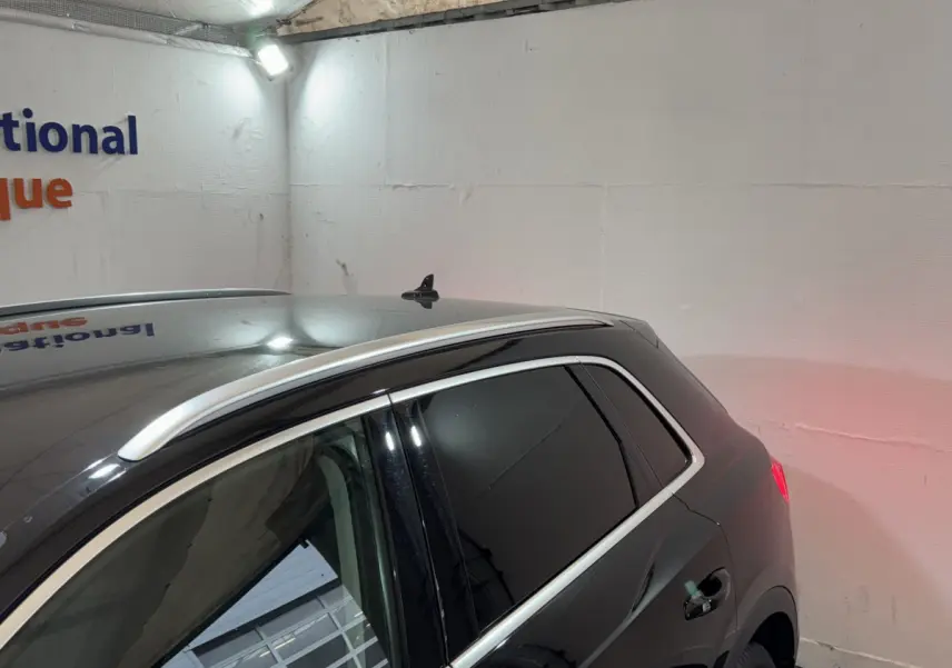 Vue latérale arrière droite d’un Audi Q3 noir avec vitres teintées et barres de toit chromées dans un garage.