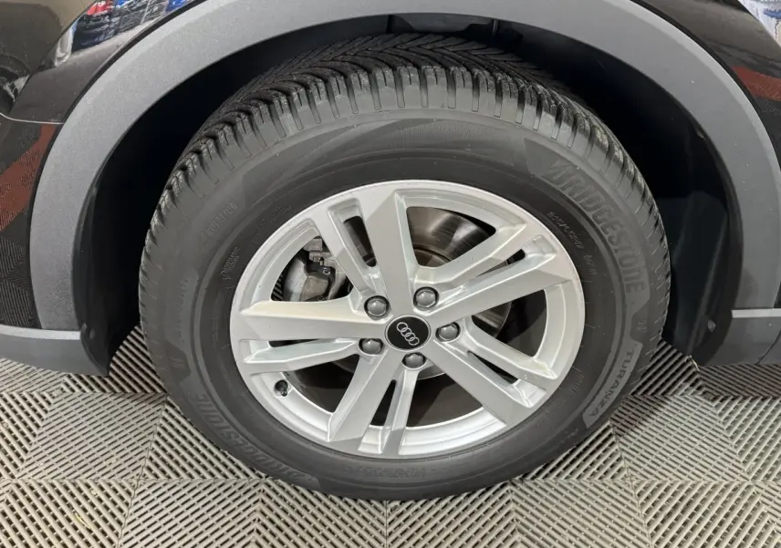 Gros plan sur la roue avant droite noire d’un Audi Q3 35 TFSI 150 MHEV avec jante argentée à 5 branches doubles.
