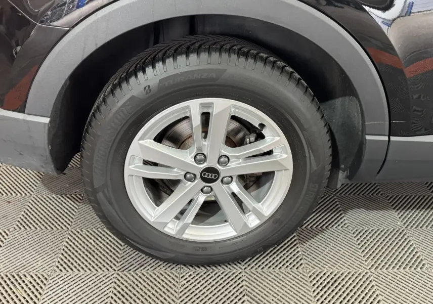 Gros plan sur la roue arrière droite d’un Audi Q3 noir, mettant en valeur la jante argentée et le pneu Bridgestone.