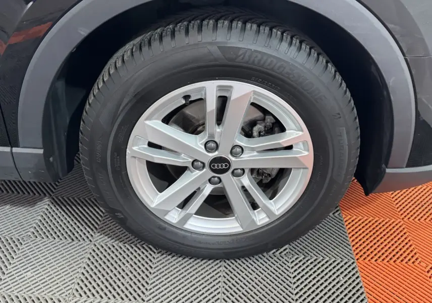 Gros plan sur la roue avant droite d’un Audi Q3 noir, avec jante alliage argentée et pneu Bridgestone.
