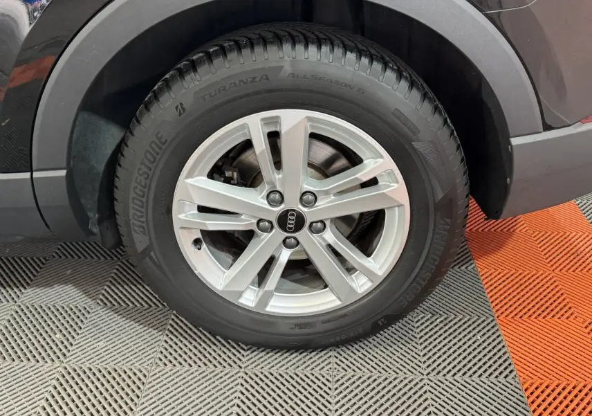 Gros plan sur la roue avant droite d’un Audi Q3 noir, mettant en valeur la jante argentée et le pneu Bridgestone.