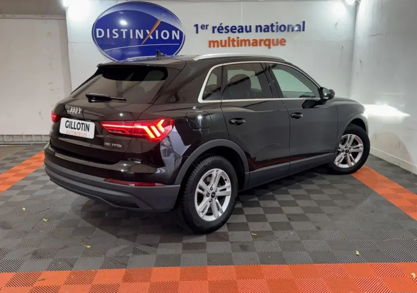 Audi Q3 noir vue 3/4 arrière droit avec feux arrière LED allumés dans un showroom intérieur.