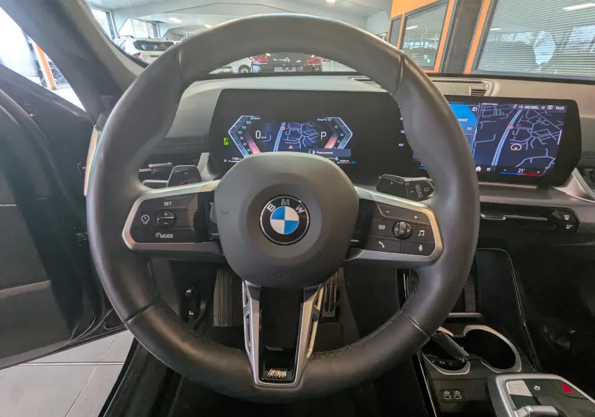 Vue intérieure centrée sur le volant cuir M de la BMW X1 noire 2025 avec tableau de bord numérique et écran GPS.