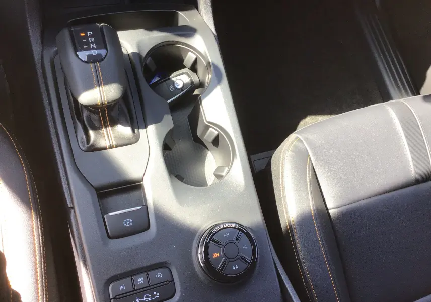 Vue rapprochée de la console centrale du Ford Ranger Wildtrak 2025, cuir noir avec surpiqûres orange et sélecteur modes 4x4.