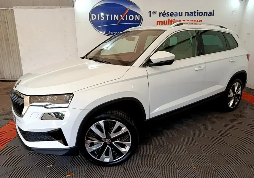 Vue 3/4 avant droite d'un Skoda Karoq blanc 2023 avec jantes alliage et barres de toit chromées.