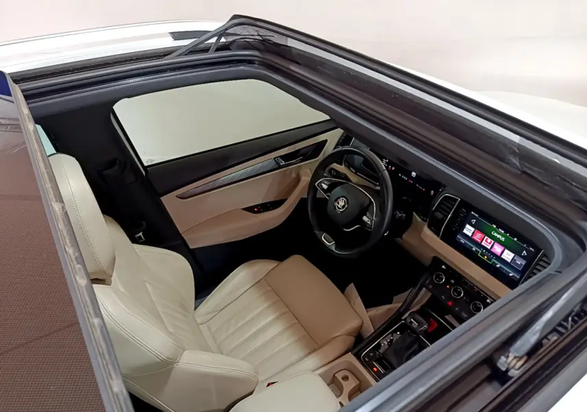 Vue plongeante sur l'intérieur beige et noir du Skoda Karoq 2023, avec tableau de bord digital et toit ouvrant.