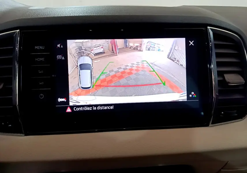 Écran tactile central montrant la caméra de recul avec alertes de distance du Skoda Karoq blanc, vue intérieure avant.