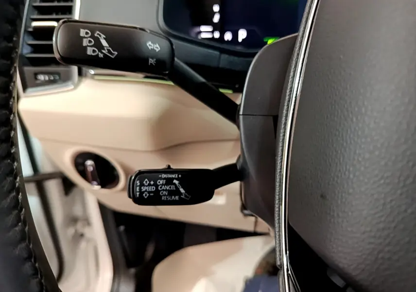 Gros plan sur les commandes au volant noir et beige du Skoda Karoq blanc, affichage digital en arrière-plan.