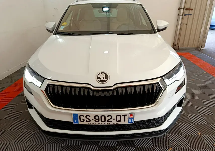 Vue avant d'un Skoda Karoq blanc 2023 avec calandre noire et phares LED allumés en intérieur.