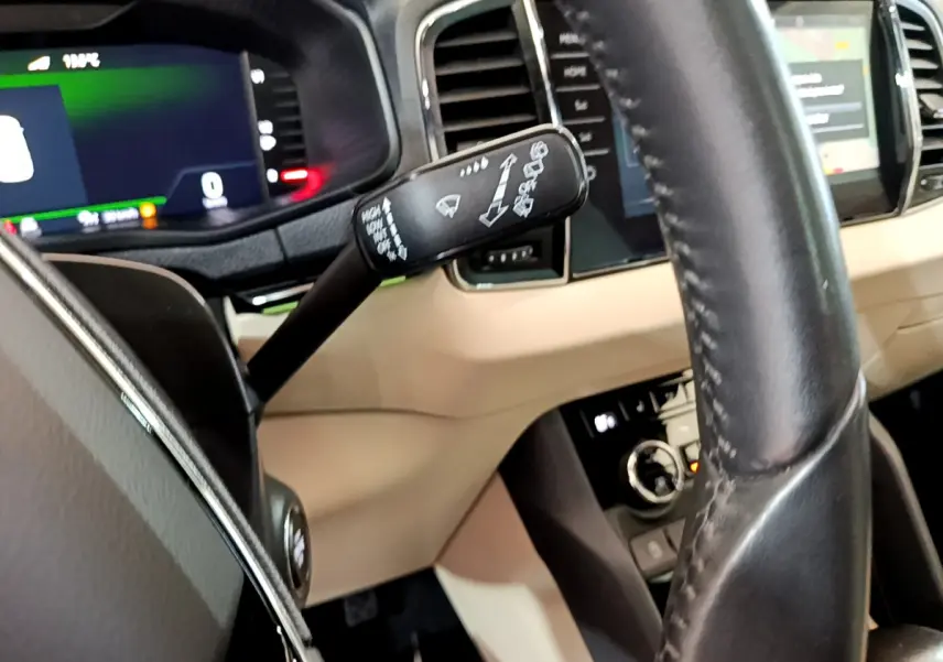 Vue rapprochée du volant noir et du tableau de bord beige du Skoda Karoq blanc, avec commandes au volant et écran tactile visible.