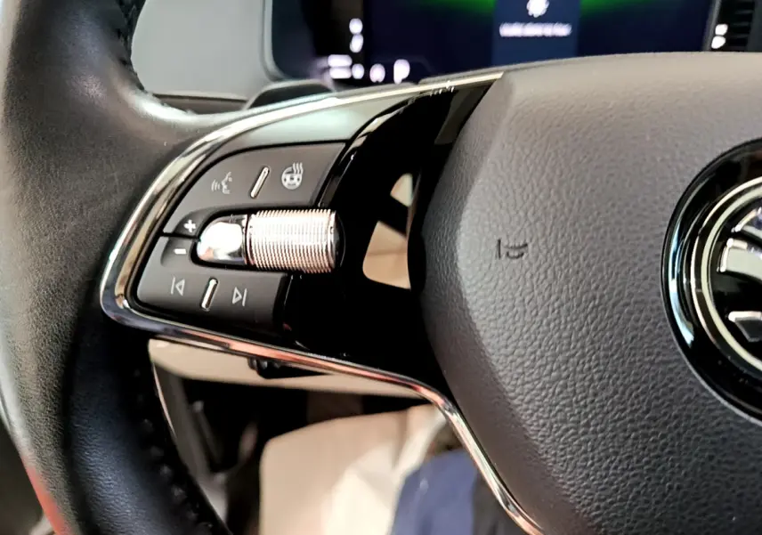 Gros plan sur le volant noir du Skoda Karoq 2023, avec commandes multifonctions et molette chromée côté gauche.