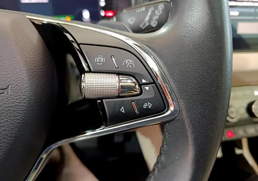 Gros plan sur les commandes du volant cuir noir du Skoda Karoq blanc, avec boutons d’aide à la conduite.