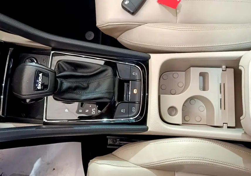 Vue plongeante sur la console centrale beige du Skoda Karoq 2023 avec levier de vitesse DSG noir et porte-gobelets intégré.