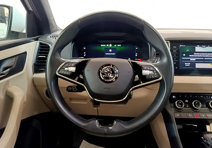 Vue frontale du volant cuir noir et du tableau de bord beige du Skoda Karoq 2023 avec écran tactile et affichage numérique.