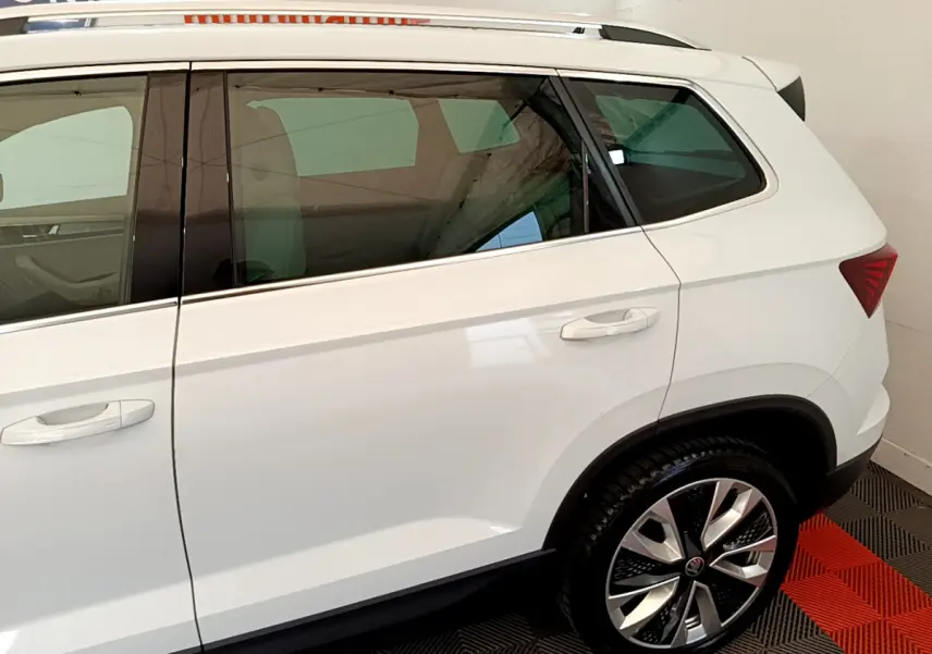 Vue latérale droite du Skoda Karoq blanc 2023, mettant en valeur la porte arrière et la roue arrière au design moderne.