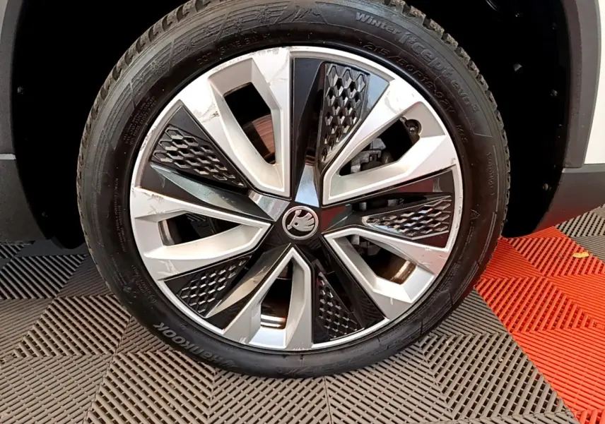 Gros plan sur la roue avant droite du Skoda Karoq blanc, mettant en valeur la jante alliage bicolore au design géométrique.