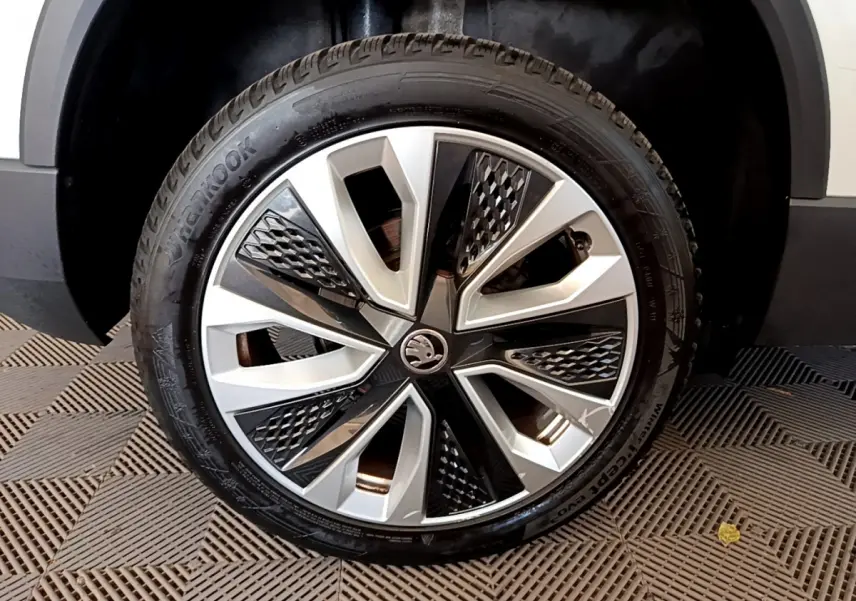 Gros plan sur la roue avant droite d’un Skoda Karoq blanc, jante alliage au design géométrique noir et argent.