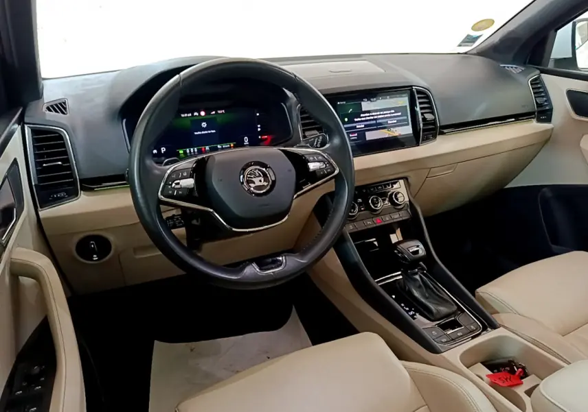 Vue intérieure avant droite du Skoda Karoq blanc, tableau de bord beige avec écran tactile et volant cuir noir.