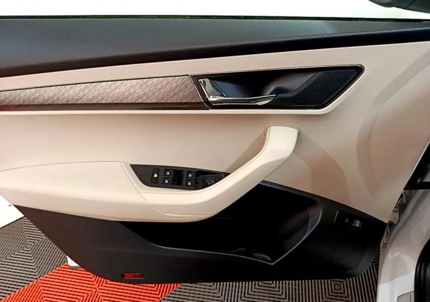 Vue côté gauche de la porte intérieure beige et noire du Skoda Karoq blanc, avec commandes de vitres et poignée chromée.
