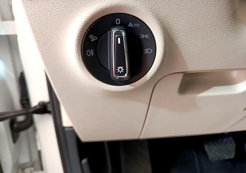 Gros plan sur la commande d’éclairage noire intégrée dans le tableau de bord beige du Skoda Karoq blanc 2023.