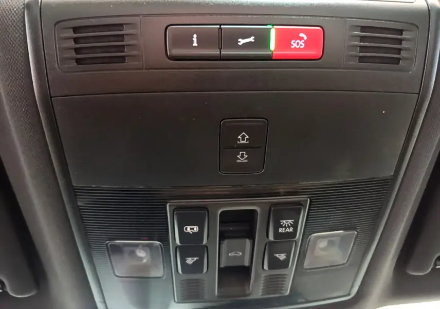 Vue en gros plan du panneau de commandes au plafond du Skoda Karoq blanc 2023, avec bouton SOS rouge et éclairage intérieur.