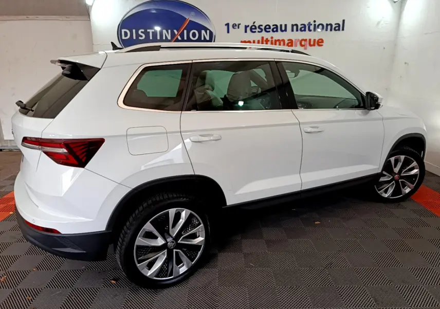 Vue latérale droite d'un Skoda Karoq blanc 2023 avec jantes alliage et vitres teintées dans un showroom.