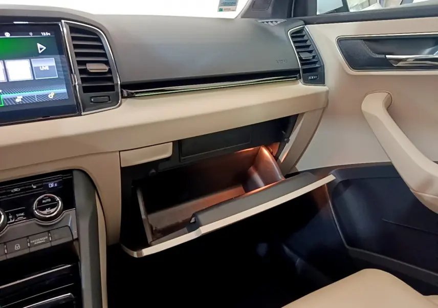 Vue intérieure côté passager du tableau de bord beige et noir d’un Skoda Karoq 2.0 TDI 116ch Style 2023 avec boîte à gants ouverte.