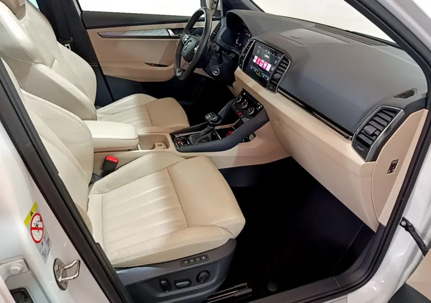 Vue intérieure côté conducteur du Skoda Karoq blanc 2023, sièges cuir beige et tableau de bord avec écran tactile.
