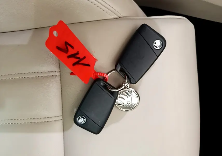 Gros plan sur deux clés noires SKODA posées sur un siège cuir beige avec un porte-clés rouge.
