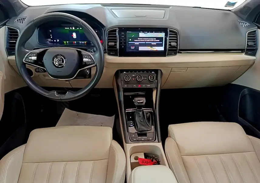 Vue intérieure frontale du Skoda Karoq 2.0 TDI 2023 avec tableau de bord beige et noir, écran tactile central et volant cuir.
