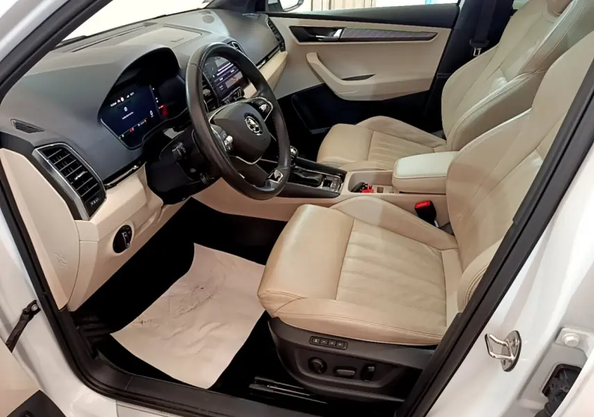 Intérieur beige clair vu côté conducteur d’un Skoda Karoq blanc, avec tableau de bord digital et volant cuir noir.