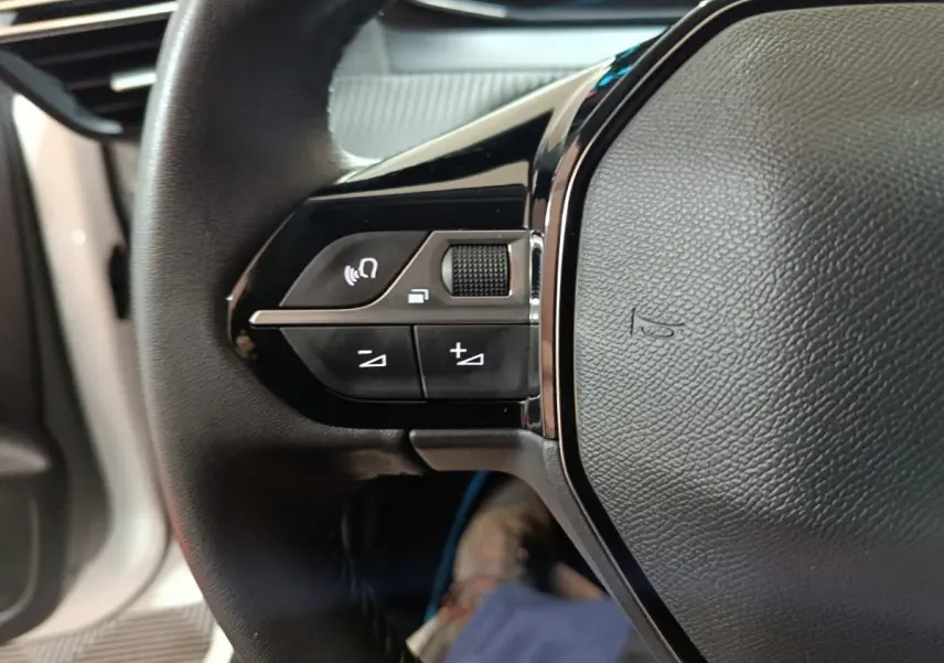 Gros plan sur les commandes gauche du volant cuir de la Peugeot 208 électrique blanche 2023 Active Pack.