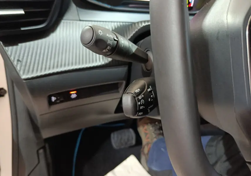 Gros plan sur les commandes au volant et tableau de bord carbone de la Peugeot 208 électrique blanche, côté conducteur.