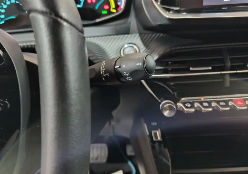 Vue rapprochée de l'intérieur de la Peugeot 208 électrique blanche, montrant le volant cuir et la commande d'essuie-glace.
