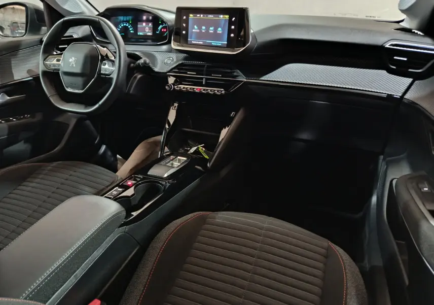 Intérieur noir de la Peugeot 208 électrique 2023 vu côté passager, avec tableau de bord numérique et écran tactile central.