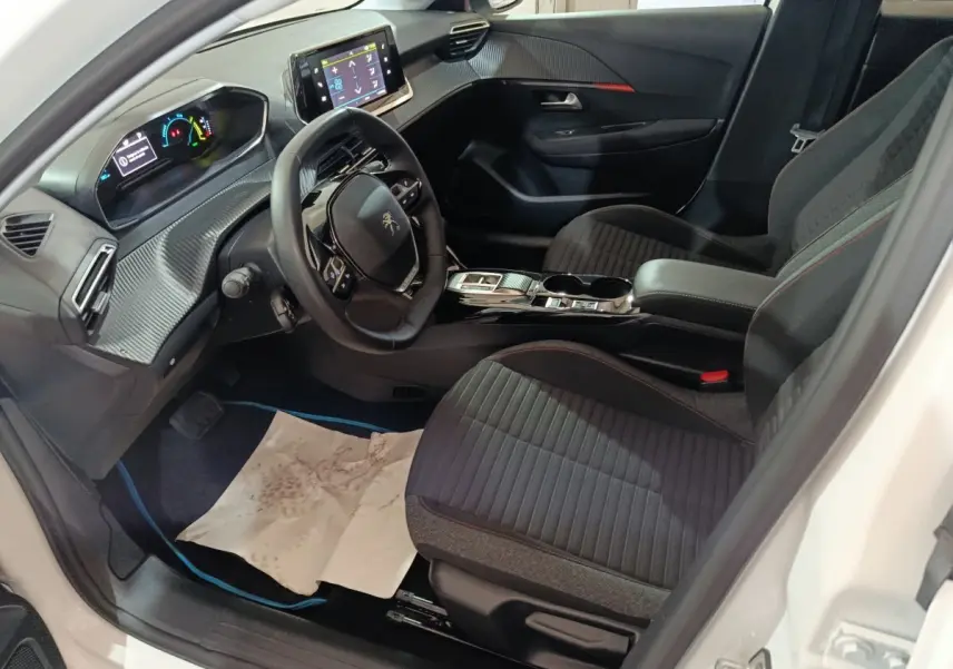 Intérieur de la Peugeot 208 électrique blanche, vue côté conducteur, avec tableau de bord digital et sièges noirs à surpiqûres rouges.