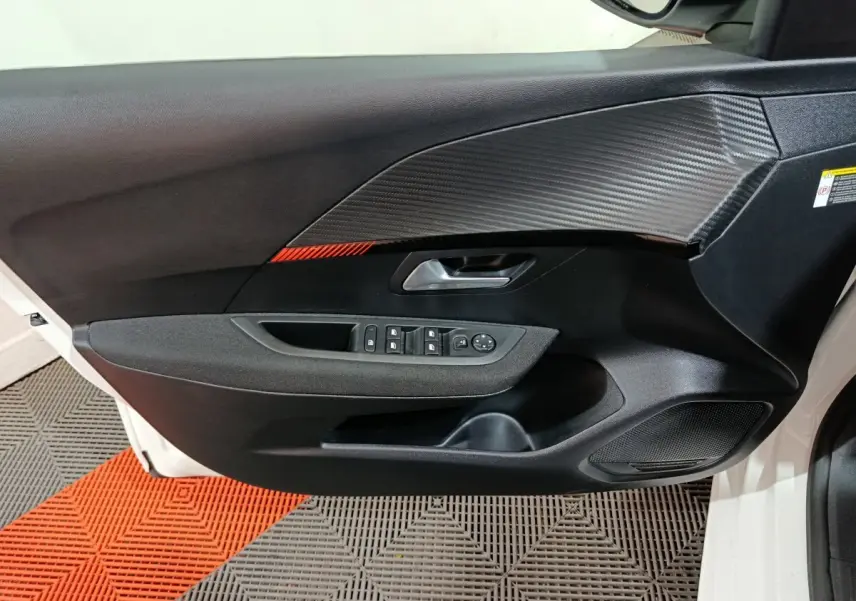 Porte intérieure côté gauche de Peugeot 208 électrique blanche 2023 avec insert carbone et bande rouge décorative.