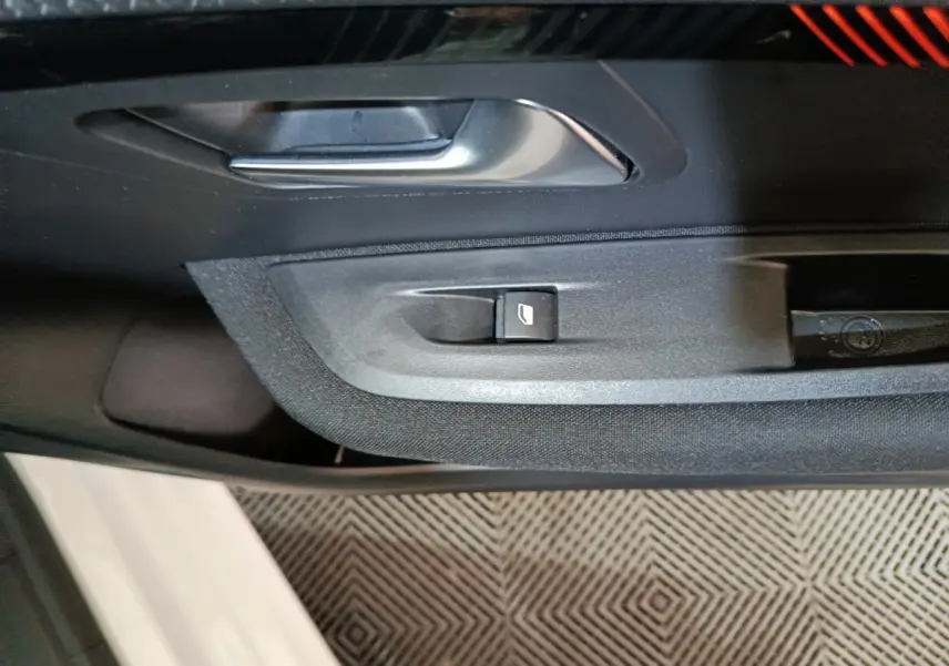 Gros plan sur la poignée intérieure et le bouton de lève-vitre côté conducteur d'une Peugeot 208 électrique blanche.