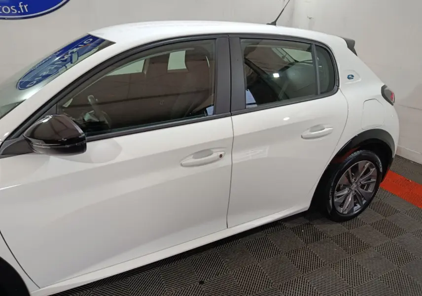 Profil côté gauche d'une Peugeot 208 électrique blanche 2023, avec rétroviseur noir et jantes alliage visibles.