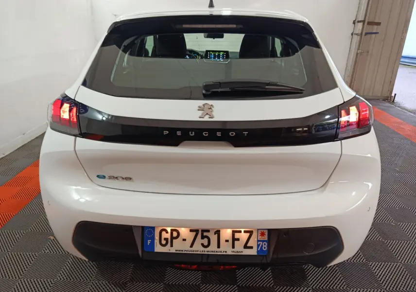 Vue arrière d'une Peugeot 208 électrique blanche de 2023 avec feux arrière LED allumés dans un garage.