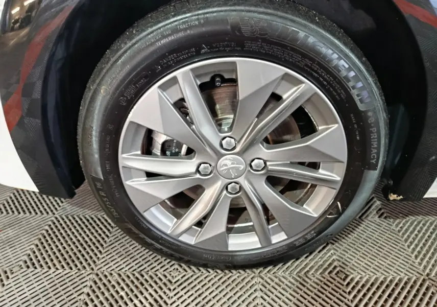 Gros plan sur la roue avant droite d'une Peugeot 208 électrique blanche, jante alliage et pneu Michelin visible.