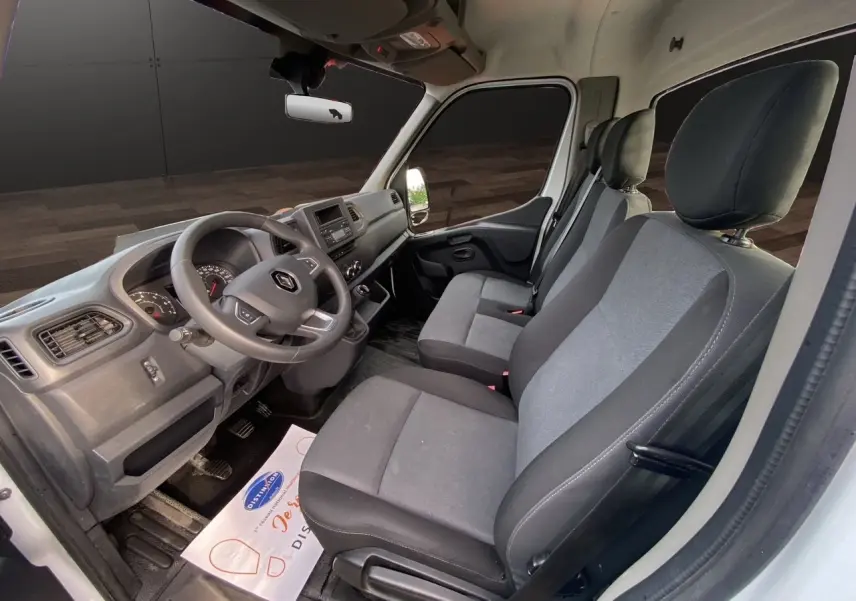 Vue intérieure côté conducteur du Renault Master 2024 blanc, montrant les sièges tissu gris et le tableau de bord fonctionnel.