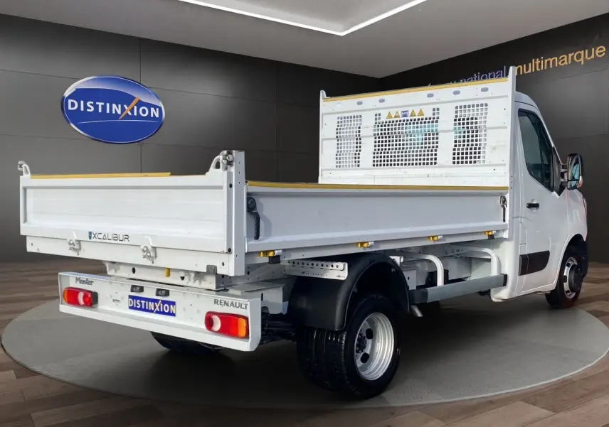 Vue 3/4 arrière droite d’un Renault Master blanc avec benne Excalibur, présenté en intérieur showroom.