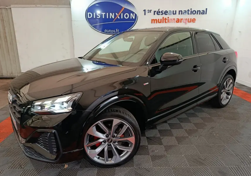 Audi Q2 35 TFSI S Line Plus noir en 3/4 avant droit, avec jantes alliage et feux LED allumés dans un showroom.