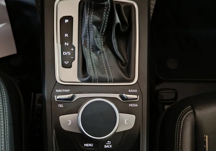 Vue plongeante sur la console centrale noire de l'Audi Q2 35 TFSI S Line Plus avec levier de vitesses et molette de contrôle multimédia.