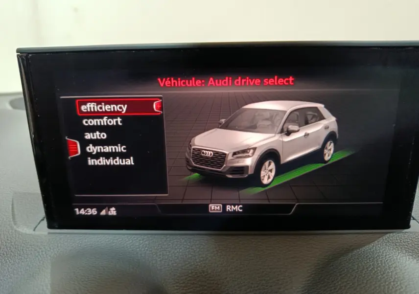 Écran intérieur montrant une Audi Q2 blanche en 3/4 avant droit avec options de mode de conduite.