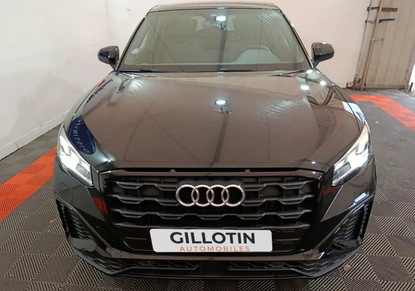 Vue frontale d'un Audi Q2 noir avec calandre noire et phares LED allumés dans un garage.