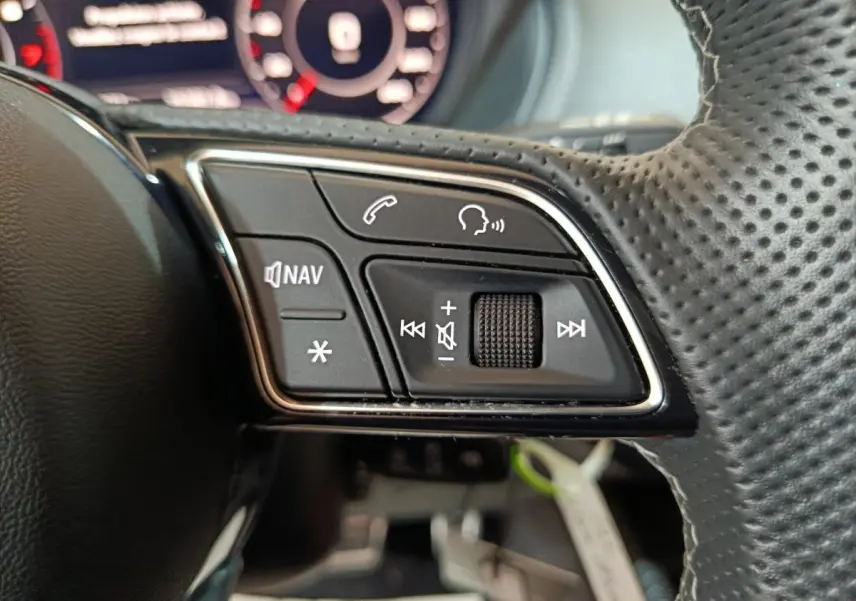 Gros plan sur les commandes gauche du volant en cuir perforé de l'Audi Q2 noir, avec boutons navigation et volume.