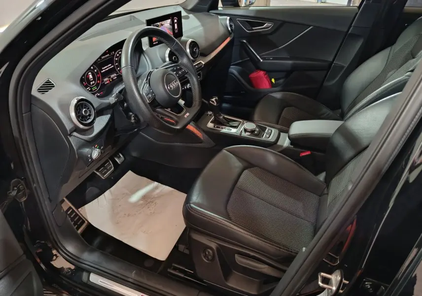 Intérieur côté conducteur d'un Audi Q2 noir 2022, avec sièges cuir noirs, volant multifonctions et tableau de bord digital.